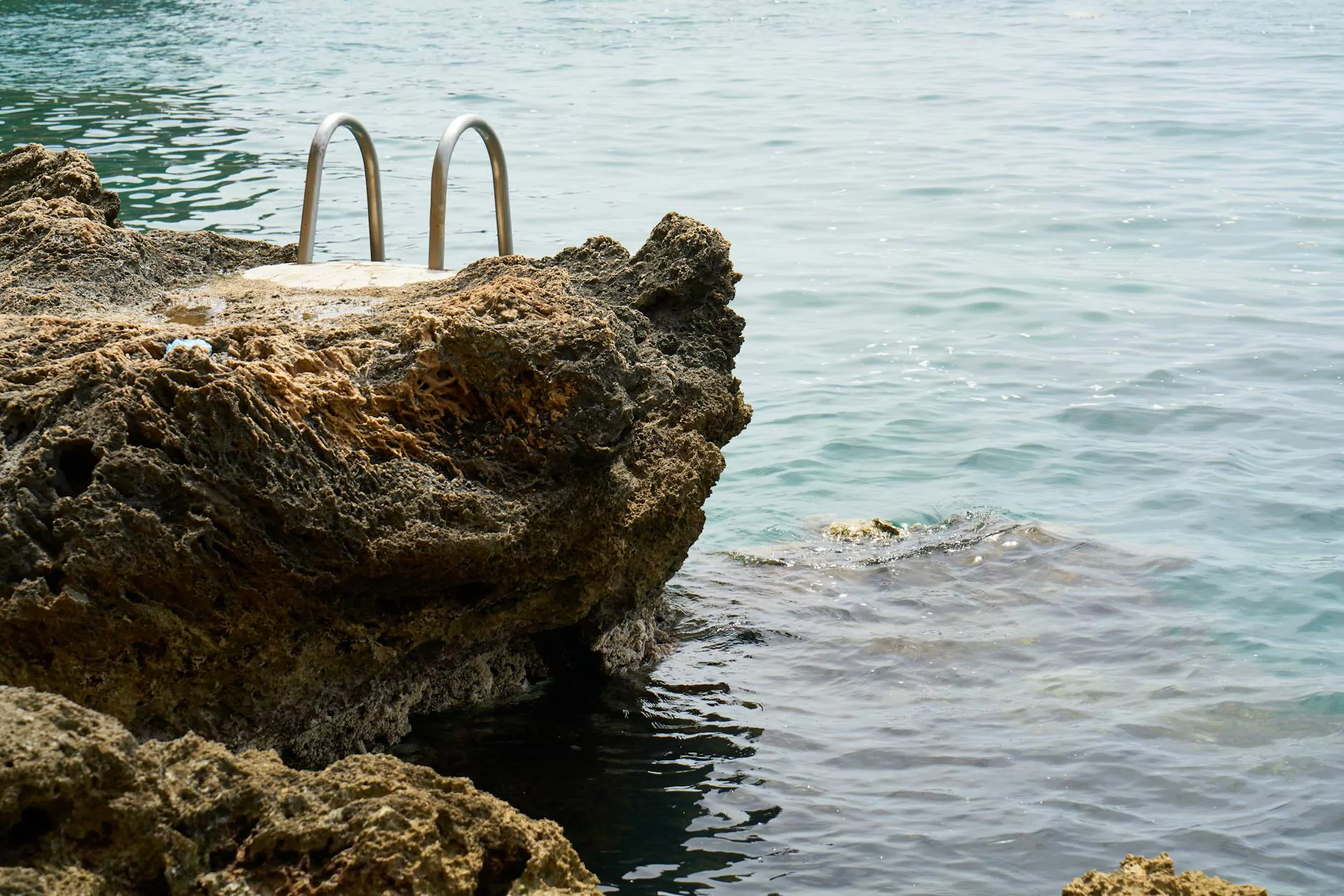 A metal swimming ladder beside a rocky shoreline and pale blue water